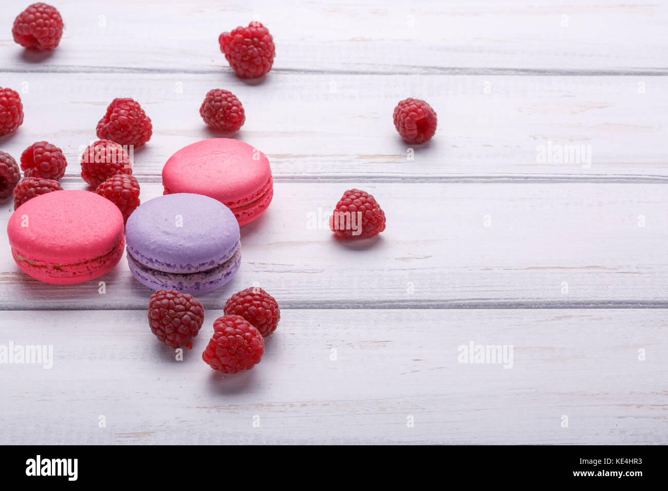 Delicious colorful biscuits macaroons with raspberries over white wooden background. Place or space for text Stock Photo