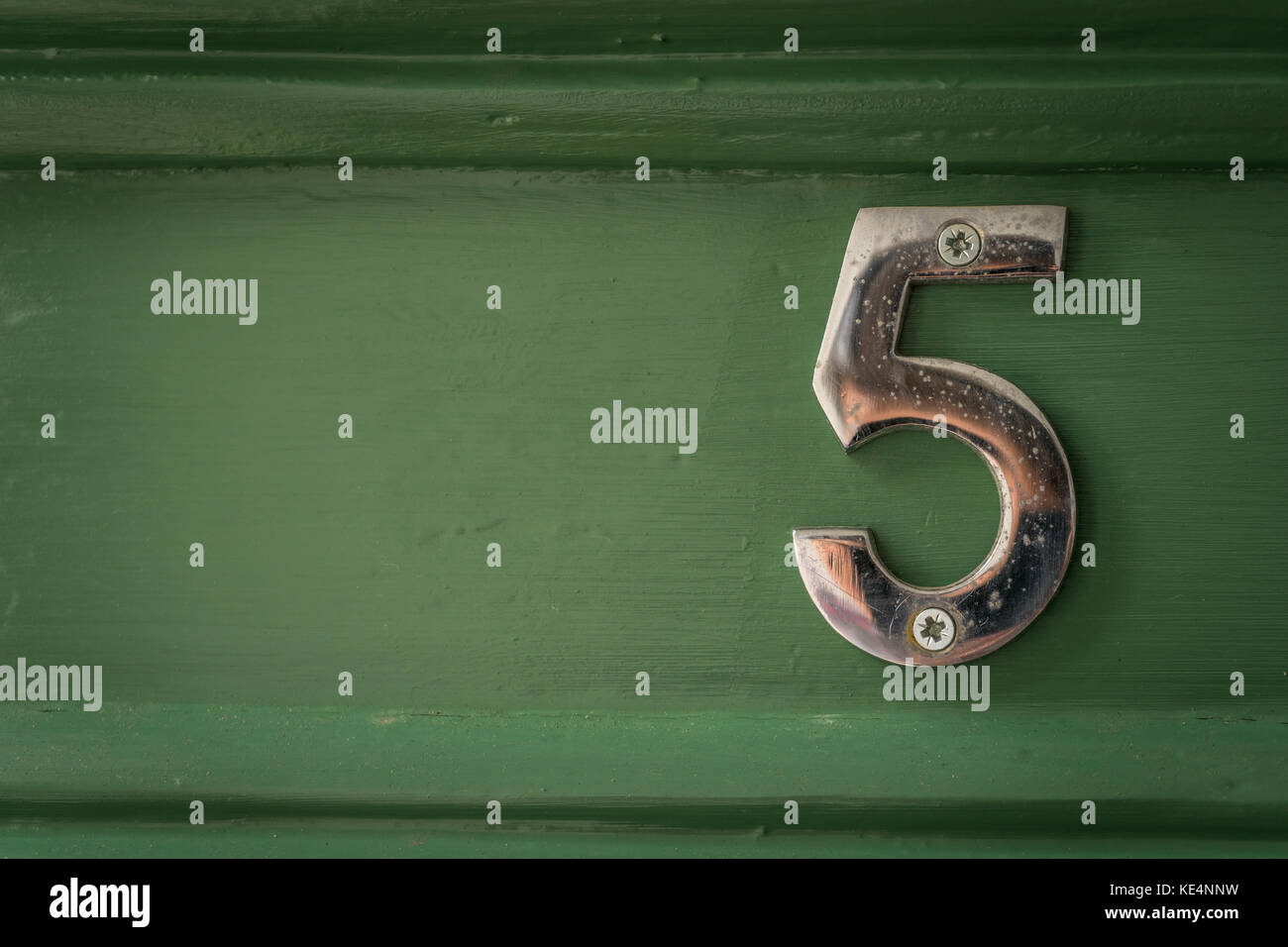 A weathered chrome number 5 screwed to a green door in the UK. Stock Photo