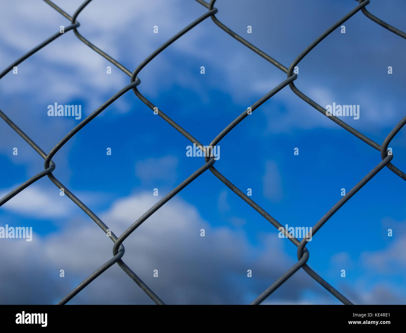 Closeup of metal fence with square units in front of dramatic blue cloudy sky. Stock Photo