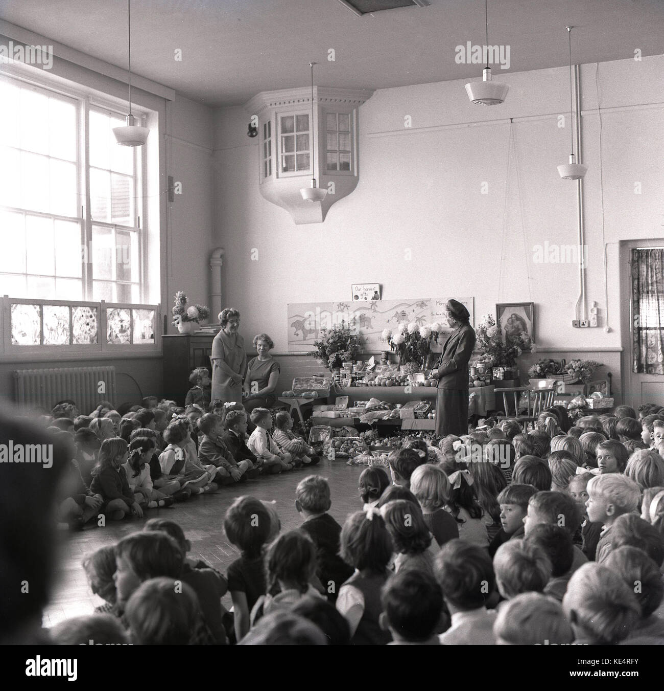 1960s, historical, Harvest thanksgiving at a christian primary school, England, UK, children sit quietly in assembly as the teacher explains the harvest and where the food they eat comes from. Stock Photo