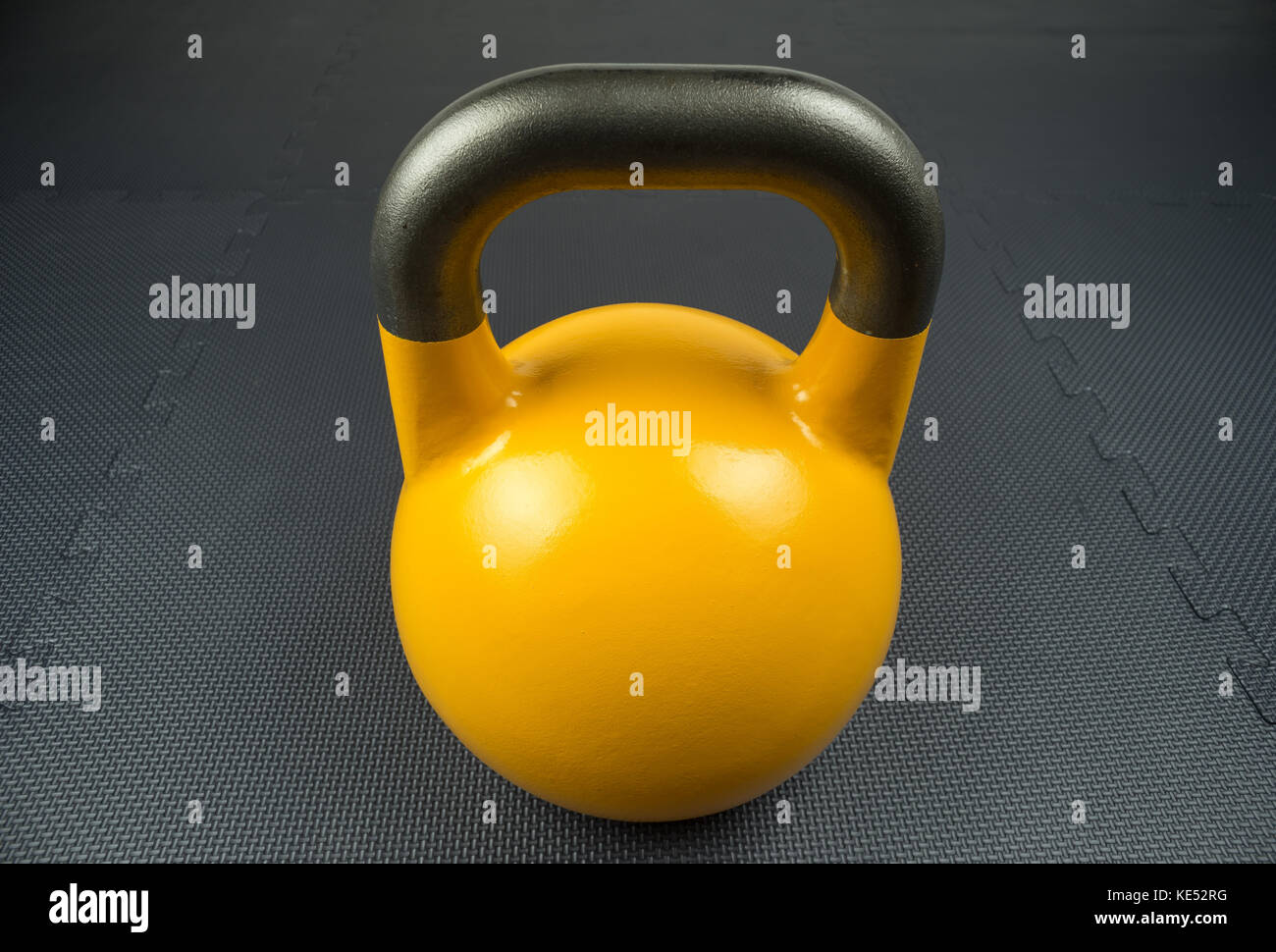 Yellow 16kg competition kettlebell on a fitness studio gym floor with rubber tiles. Potential text / writing space at center of kettlebell. Stock Photo