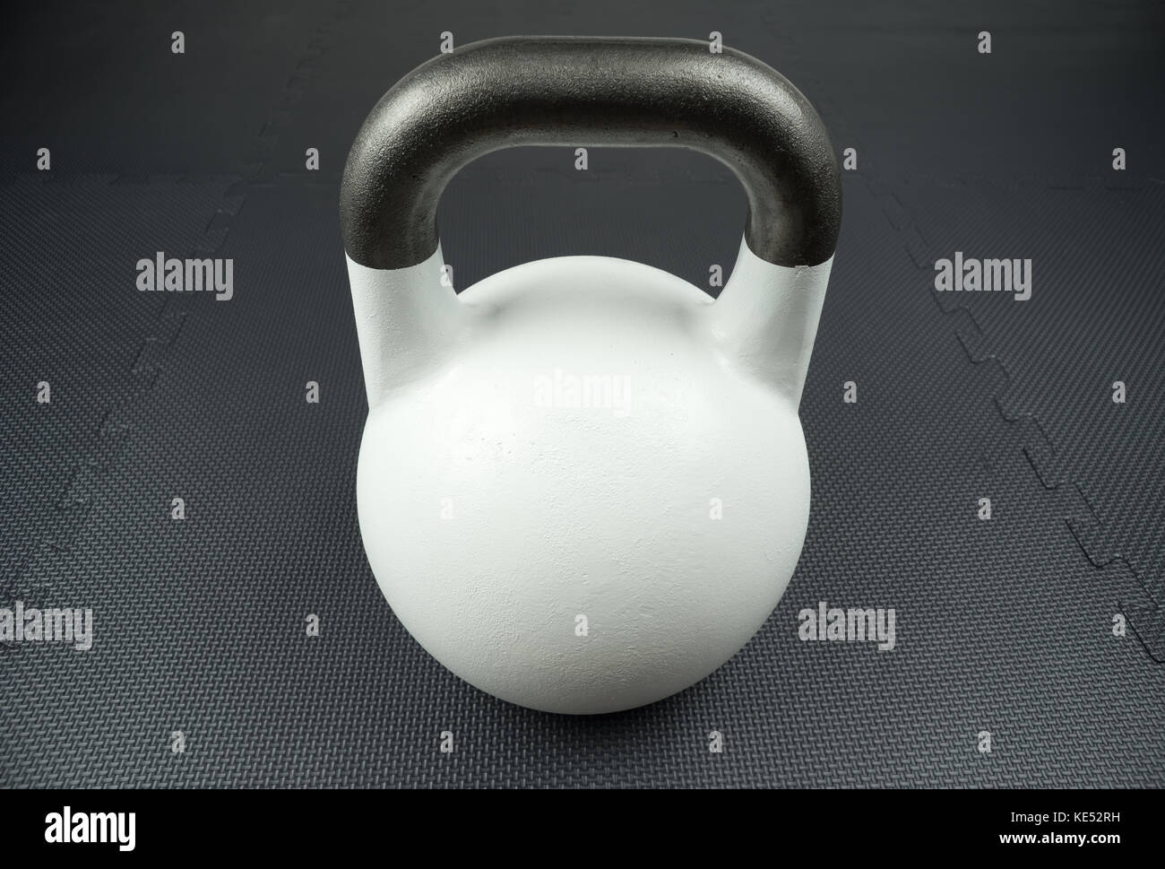White 10kg competition kettlebell on a fitness studio gym floor with rubber tiles. Potential text / writing space at center of kettlebell. Stock Photo