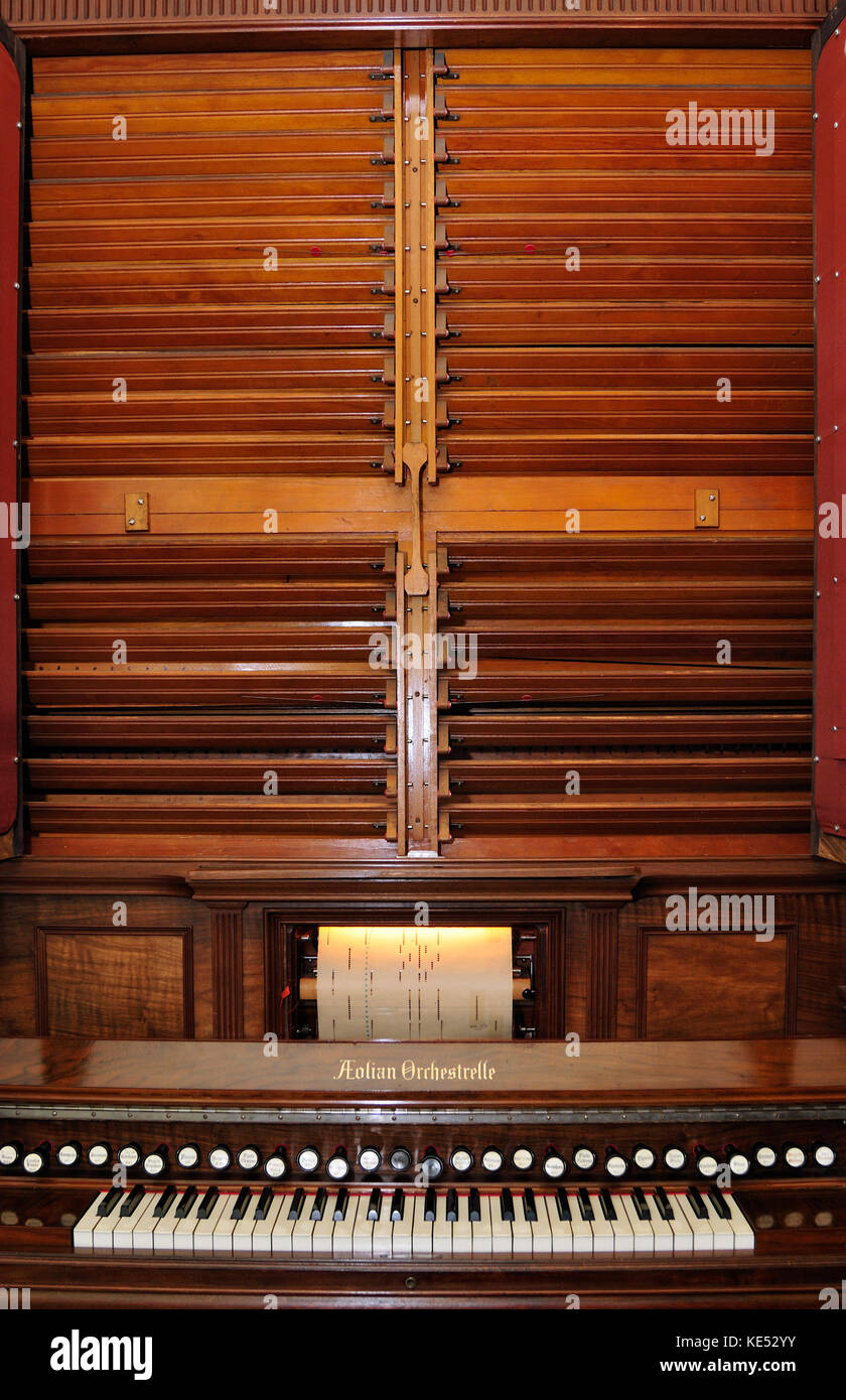 Aeolian Orchestrelle - Louvres behind doors increase volume. 'Model Y' made by Aeolian Orchestrelle Company of New York  in 1901. Height 8 foot, 4 inches, width 6 foot 4 inches.  Utilises 28 stops and cost £600 when first new. Case made from walnut, interior from yellow tulipwood.  Plays paper rolls automatically and can be played manually using keyboard.  Air is pumped by an electric blower.  2 wooden levers are knee or hand operated. Piano roll is a roll of paper with perforations (holes) punched in it.Produced industrially. Stock Photo