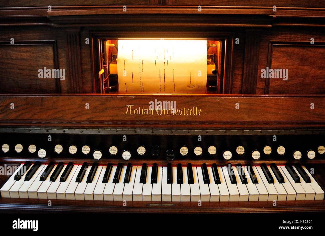 Aeolian Orchestrelle -  paper player with perforated piano roll 'Model Y' made by Aeolian Orchestrelle Company of New York  in 1901. Height 8 foot, 4 inches, width 6 foot 4 inches.  Utilises 28 stops and cost £600 when first new. Case made from walnut, interior from yellow tulipwood.  Plays paper rolls automatically and can be played manually using keyboard.  Air is pumped by an electric blower.  2 wooden levers are knee or hand operated. Piano roll is a roll of paper with perforations (holes) punched in it.Produced industrially. Laguna roll of Moonlight Intermezzo by E H Lemare. Stock Photo