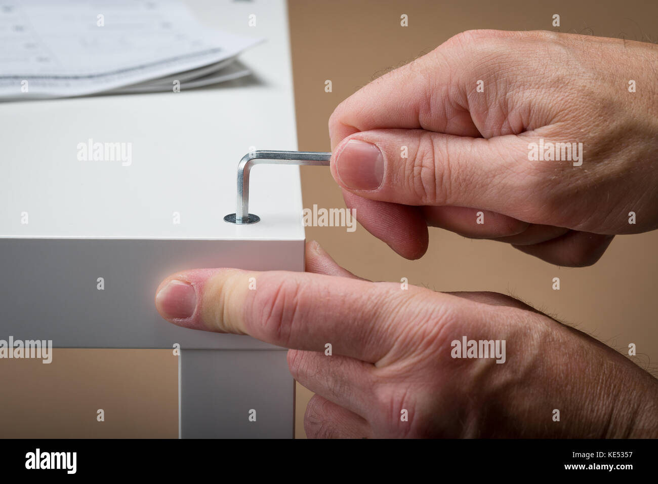 A man building flat pack furniture using an allen Key with the building instructions in the background Stock Photo