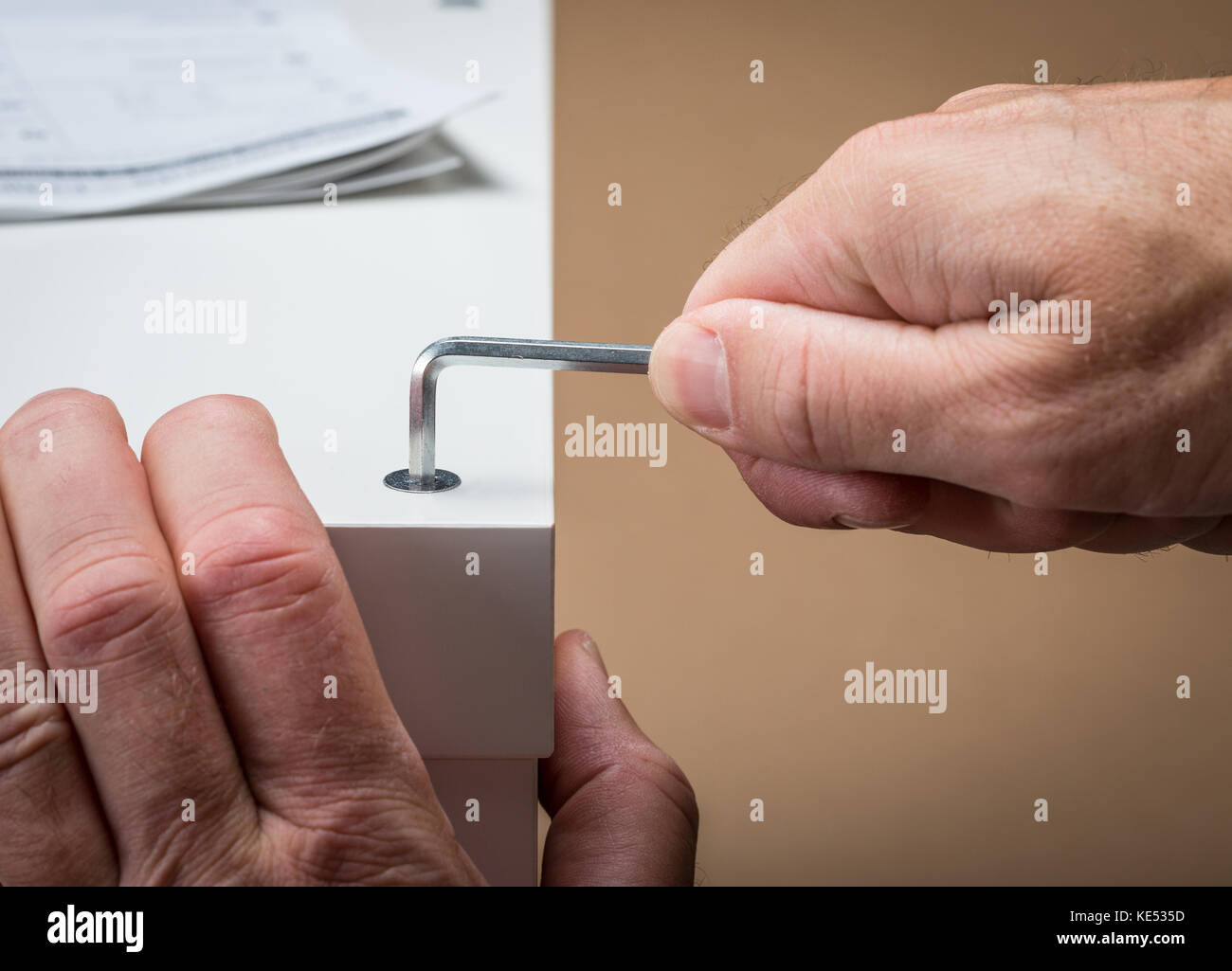 A man building flat pack furniture using an allen Key with the building instructions in the background Stock Photo