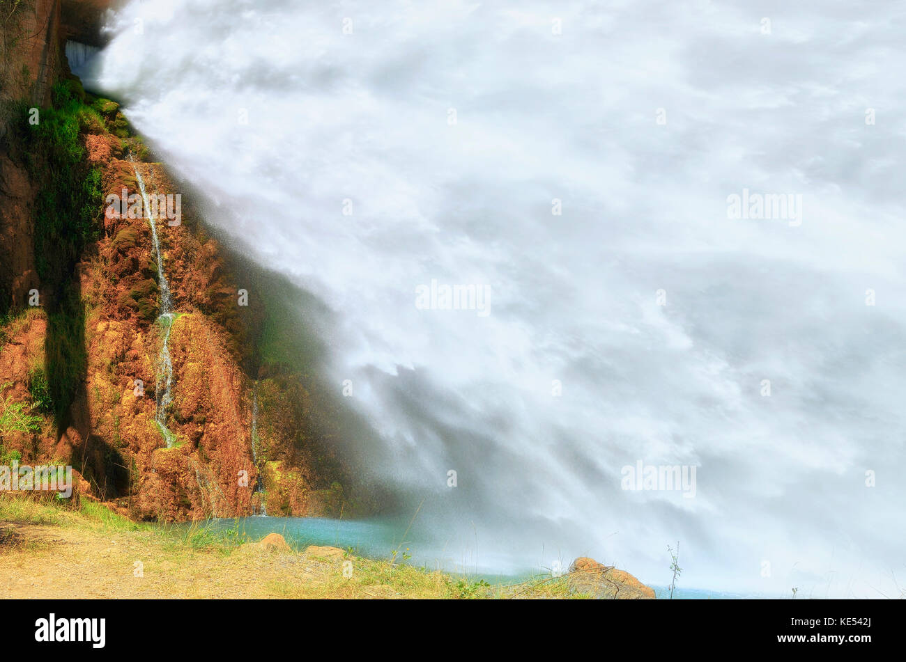 Big artificial waterfall. Near of the spillway, in a hydroelectric dam. Water flowing, strongly, towards a river. Beautiful colorful landscape. Stock Photo