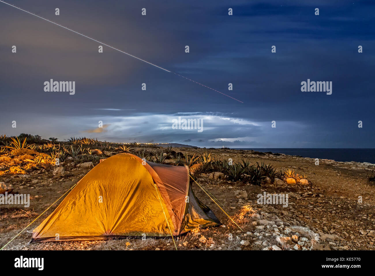 A camping tent set up during a thunderstorm, with aircraft trails in