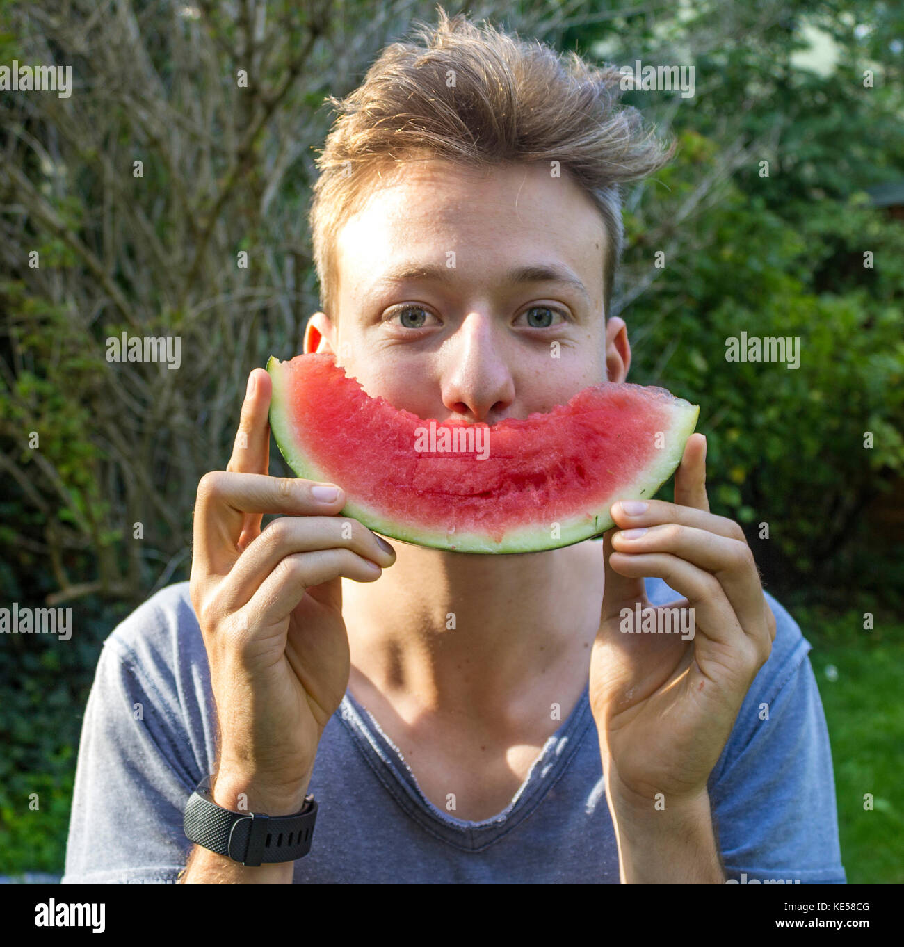 Young man holding a melon as mouth in front of his face, Bavaria, Germany Stock Photo