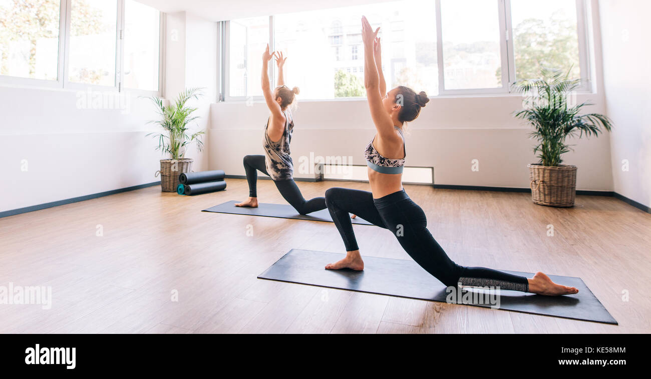 Two young people working out indoors. Fitness class doing yoga.  Man and woman stretching forward in warrior pose. Stock Photo