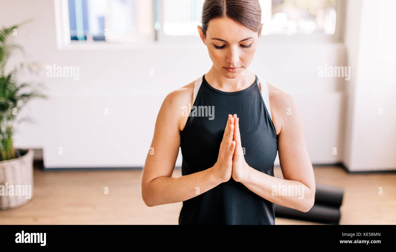 fitness female meditating with her eyes closed and hands joined indoors. Woman in easy posture with Namaste, meditating, breathing and relaxing. Stock Photo