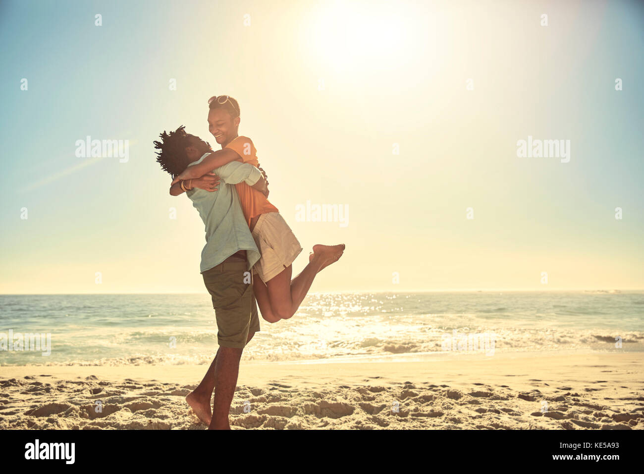 Playful boyfriend lifting girlfriend on sunny summer ocean beach Stock Photo