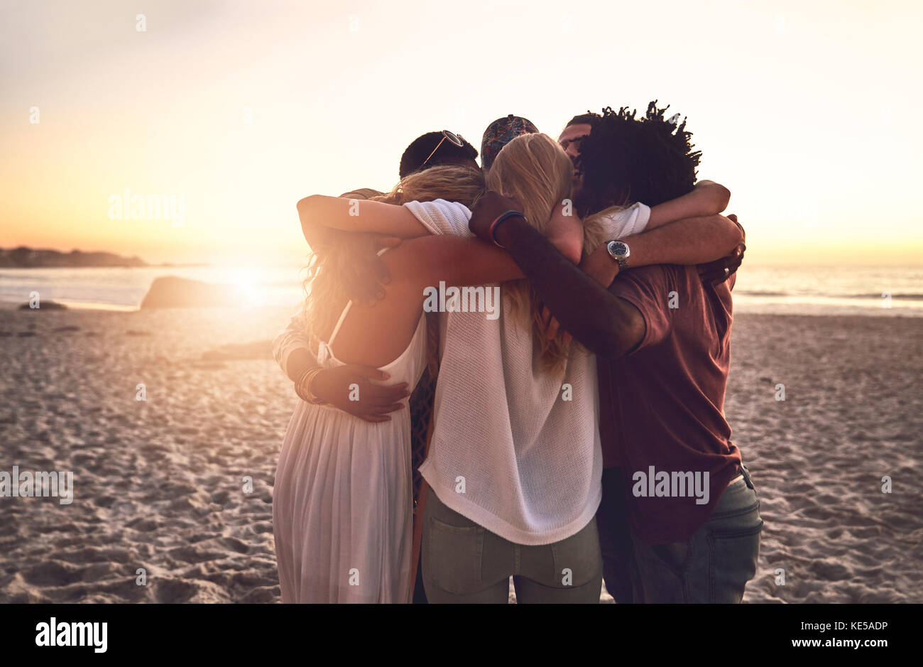 Young friends hugging in a huddle on sunset summer beach Stock Photo