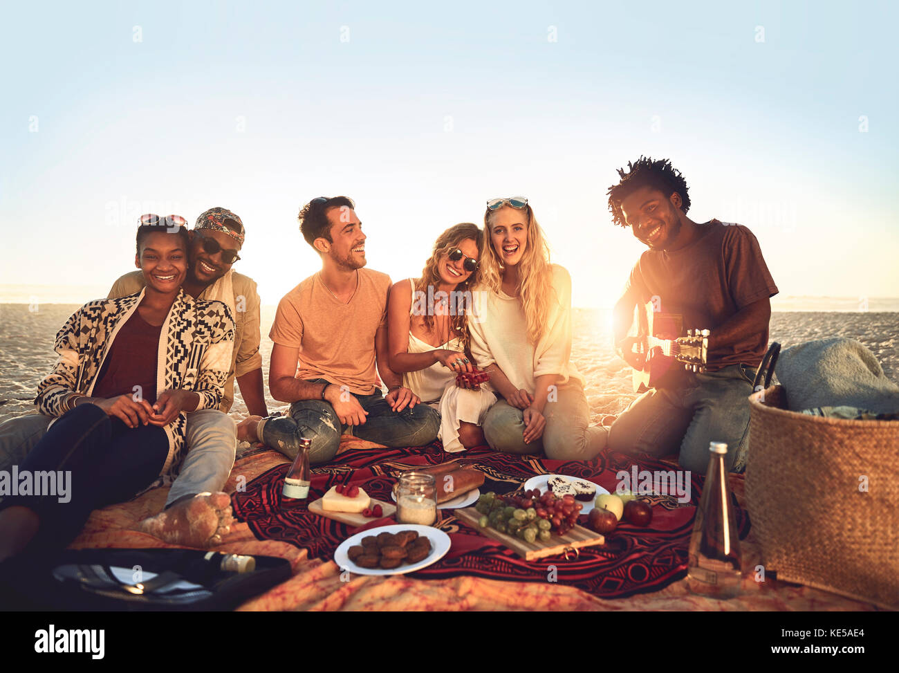 Portrait young friends hanging out, enjoying picnic on sunny summer beach Stock Photo