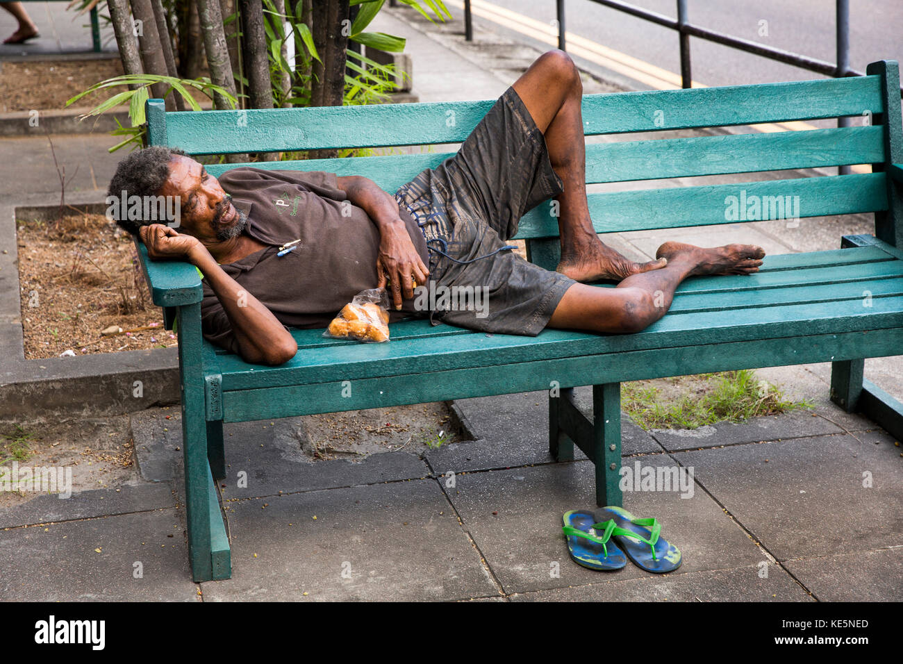 The Seychelles, Mahe, Victoria, Revolution Avenue, poor Seychellois man asleep on roadside bench Stock Photo