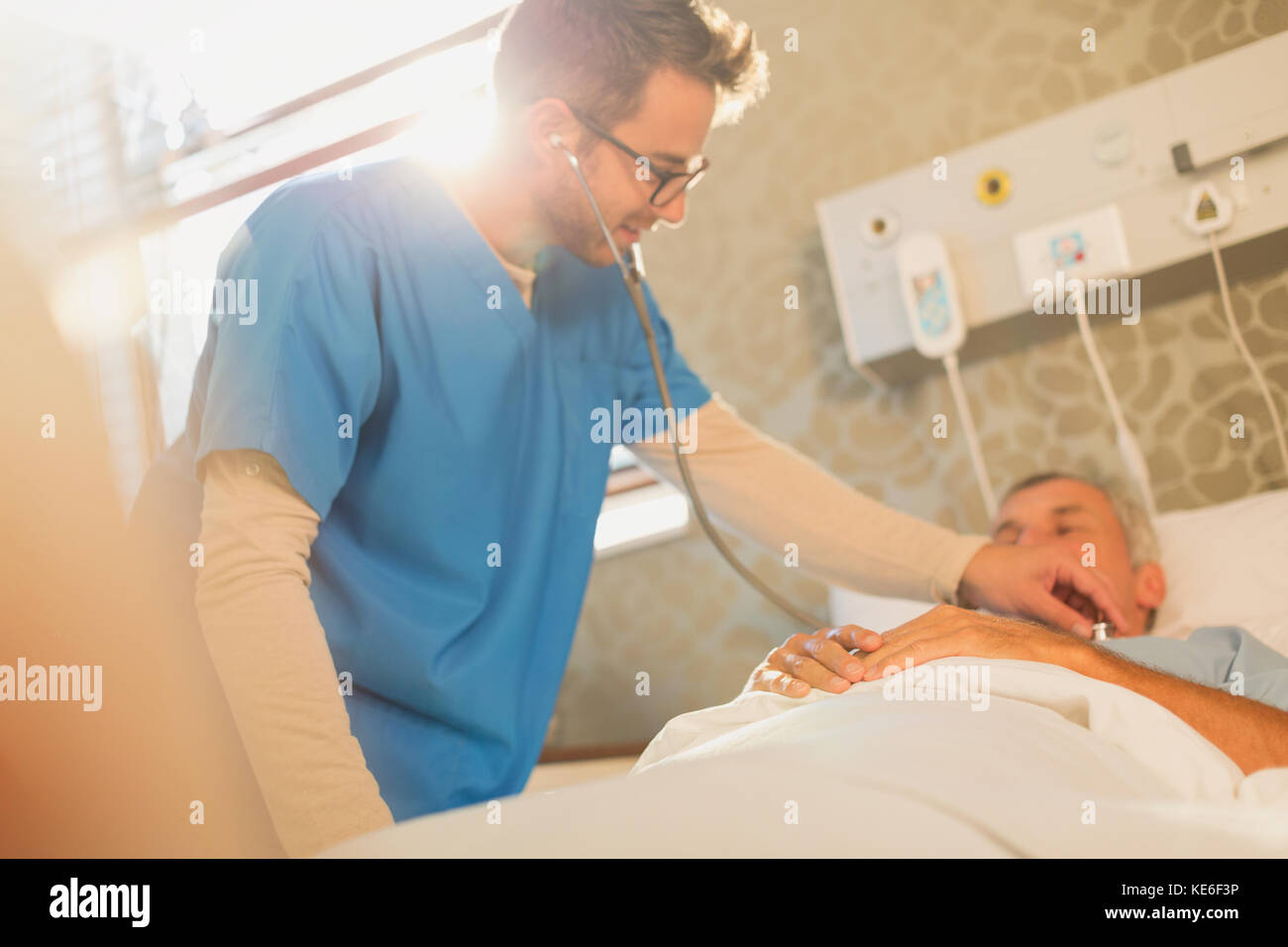 Male nurse using stethoscope on patient in hospital bed Stock Photo