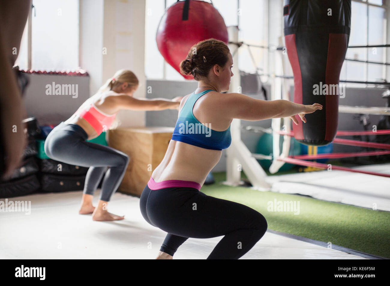 Young women doing squats next to boxing ring in gym Stock Photo