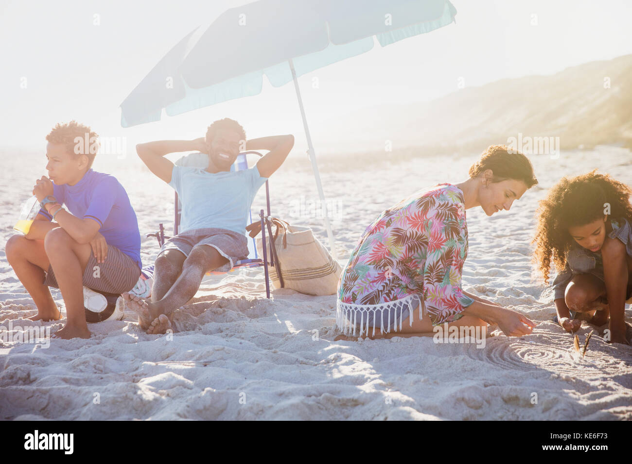 Multi-ethnic family relaxing and playing in sand on sunny summer beach Stock Photo