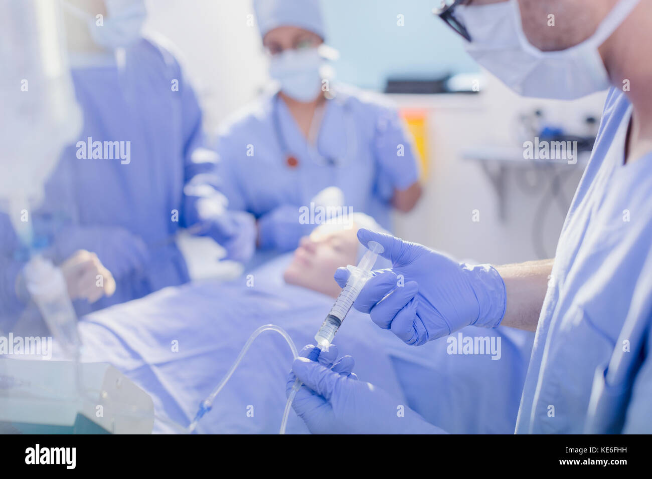 Anesthesiologist with syringe injecting anesthesia into IV drip in operating room Stock Photo