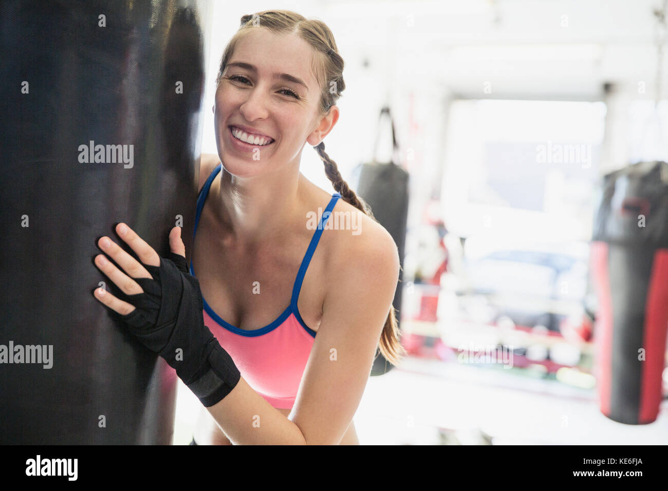 Portrait smiling, confident young female boxer at punching bag in gym Stock Photo