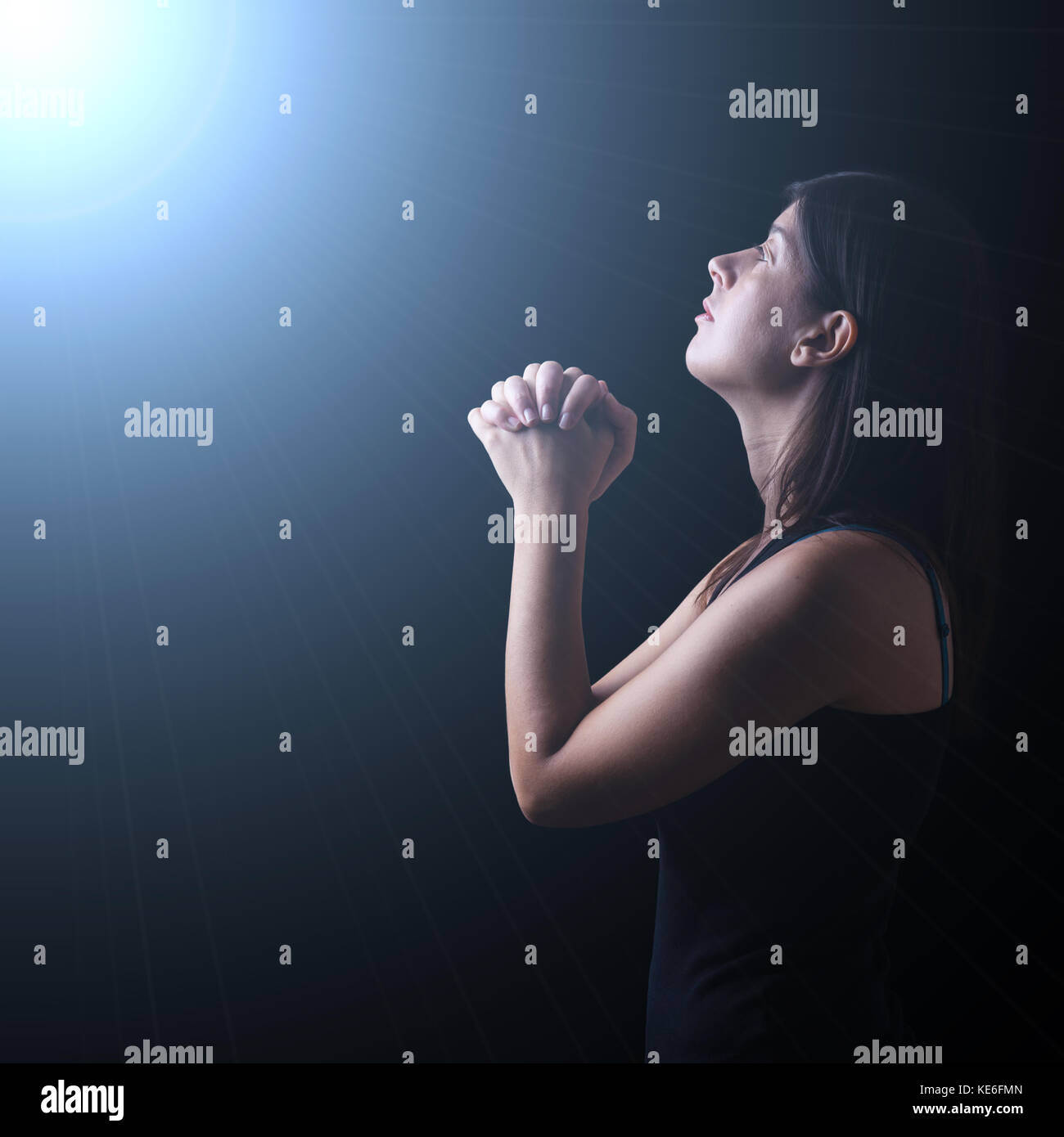 Faithful woman praying in worship to god looking up in hope, under a divine or celestial light. faith prayer spirituality prayer heavenly iluminated Stock Photo