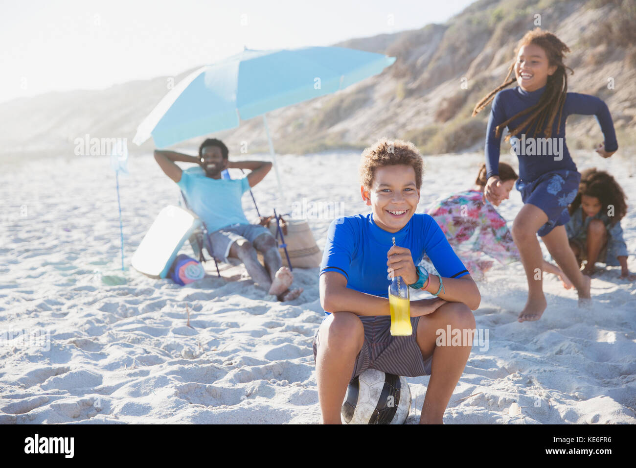 Portrait smiling pre-adolescent boy drinking juice on sunny summer beach with family Stock Photo