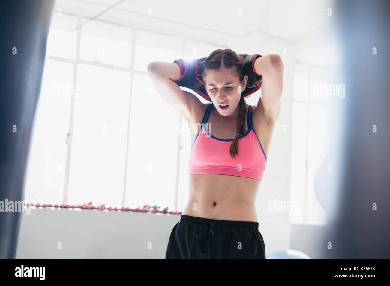 Tired young female boxer resting with hands behind head in gym Stock Photo