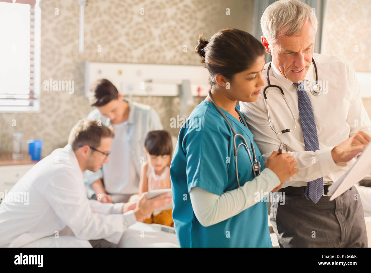 Male doctor and female nurse making rounds, reviewing medical record in hospital room Stock Photo
