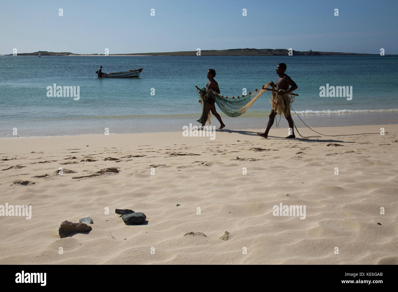 Two fishermen walking on a beach in Cape Verde island holding a fishing net  with a small fishing boat in the background Stock Photo - Alamy