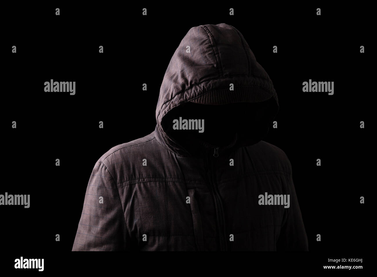 Scary and creepy man hiding in the shadows, standing in the darkness / black background hood hiding face shadows dangerous mysterious stalker hood Stock Photo