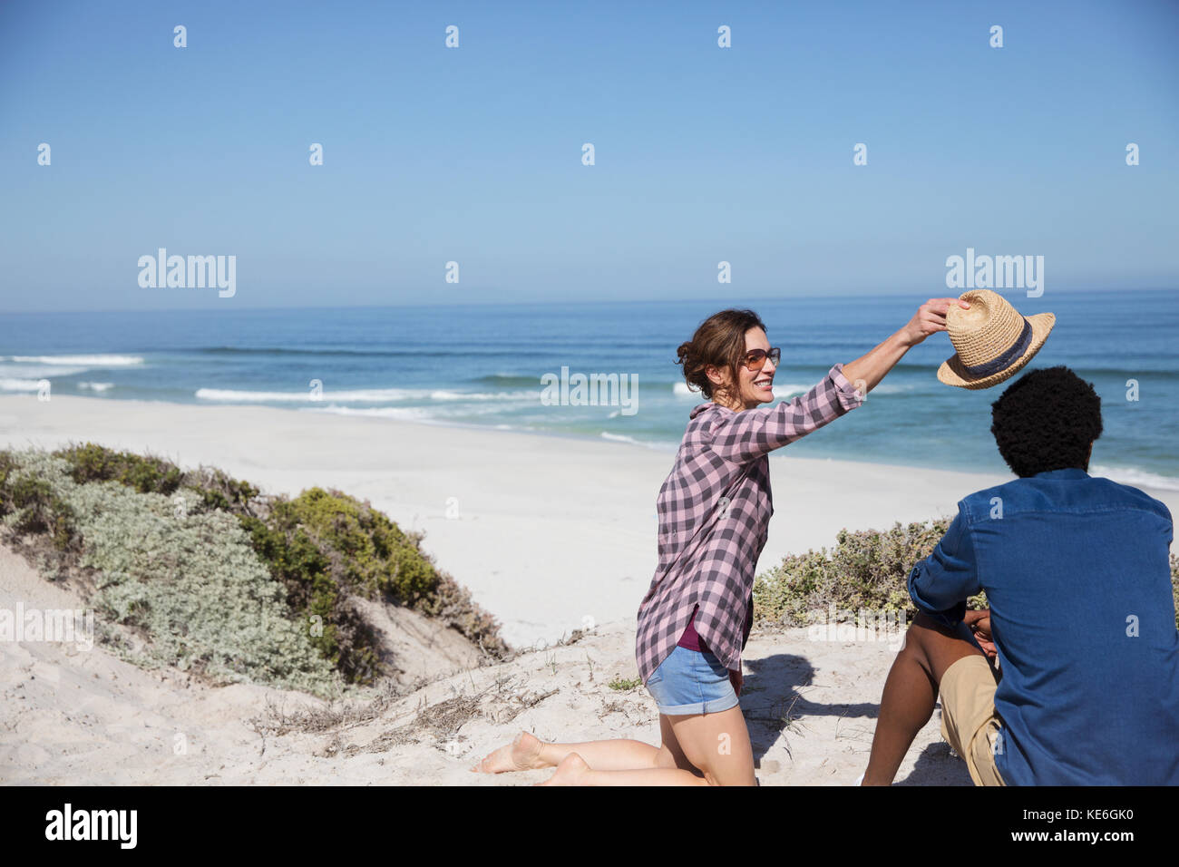 Woman placing hat on boyfriend on sunny summer ocean beach Stock Photo