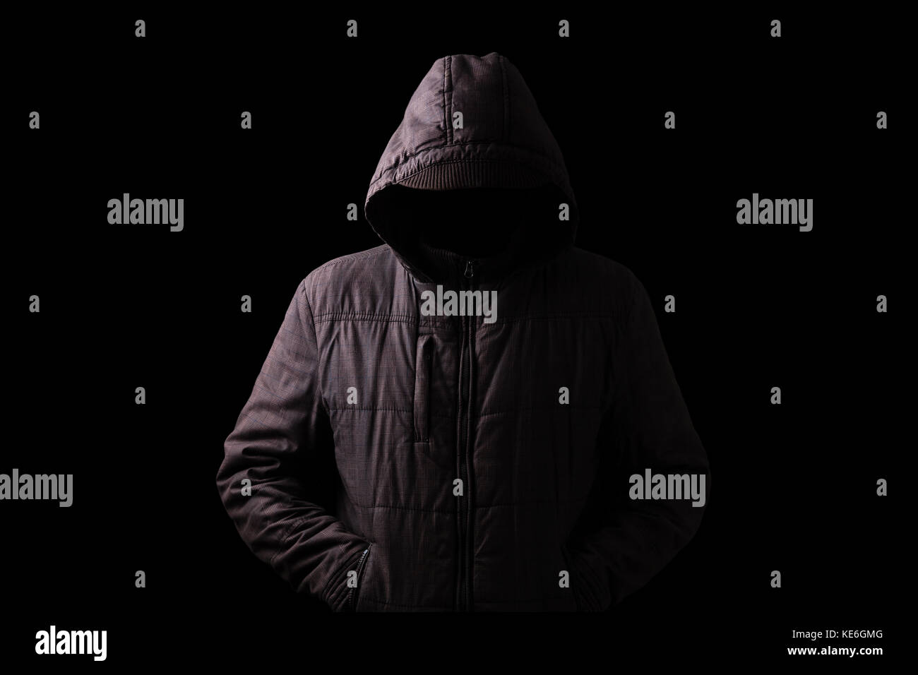 Scary and creepy man hiding in the shadows, standing in the darkness / black background hood hiding face shadows dangerous mysterious stalker hood Stock Photo