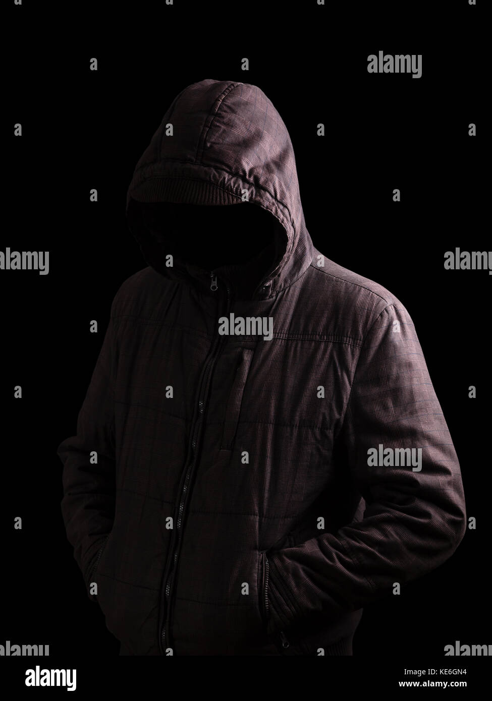 Scary and creepy man hiding in the shadows, standing in the darkness / black background hood hiding face shadows dangerous mysterious stalker hood Stock Photo