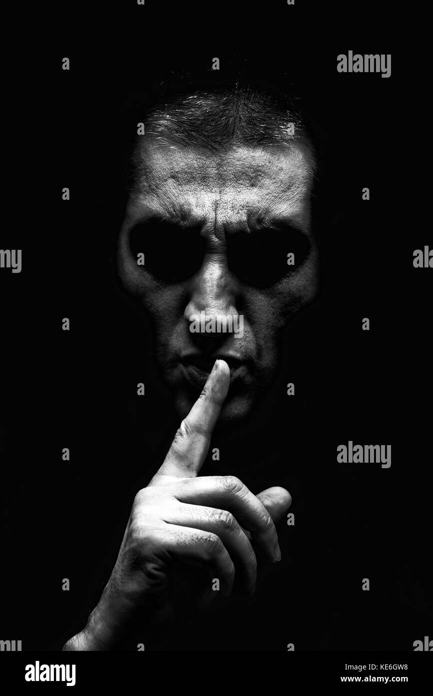 Angry mature man with aggressive look making silence sign in threatening and creepy way. Black background / shh shhh shut up scary creepy angry secret Stock Photo