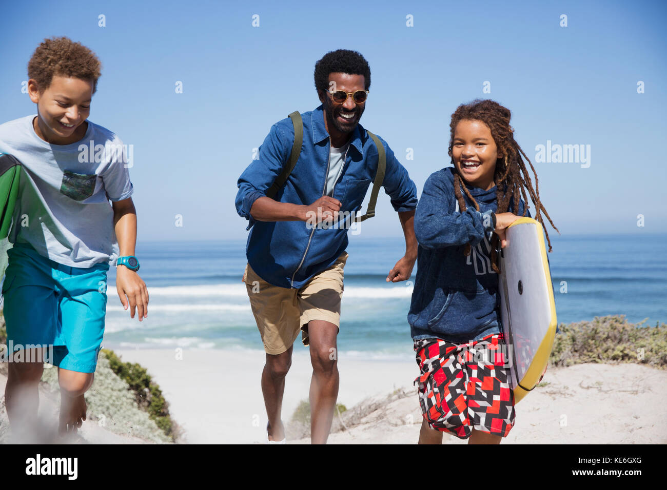 Playful family with boogie board running on sunny summer beach Stock Photo