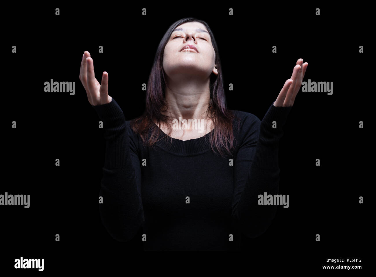 Mourning woman praying with arms outstretched in worship to god. Looking up, eyes closed in suffering. Black background / faith sad grief mourning Stock Photo