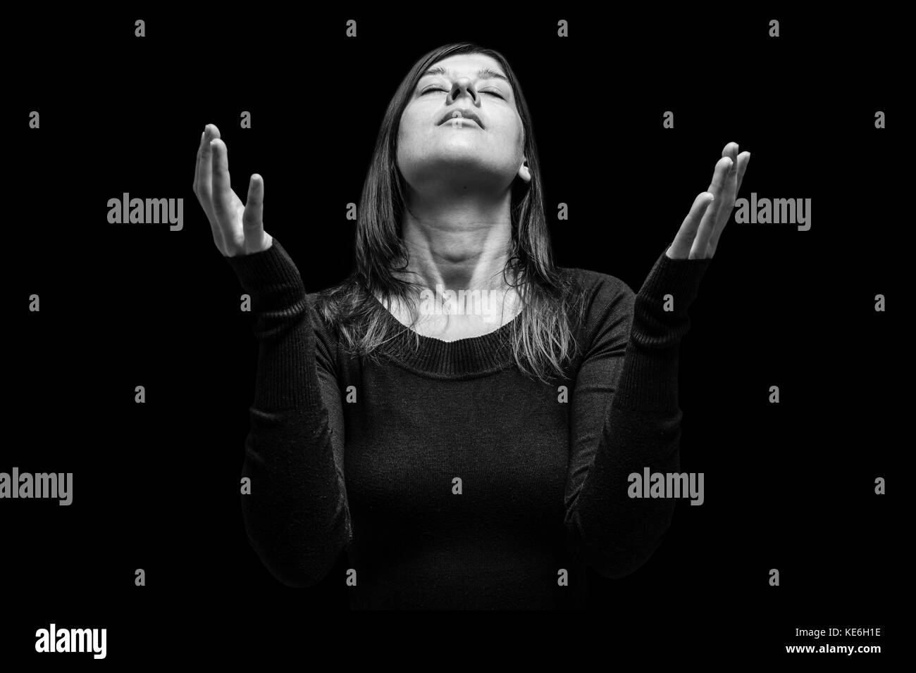Mourning woman praying with arms outstretched in worship to god. Looking up, eyes closed in suffering. Black background / faith sad grief mourning Stock Photo