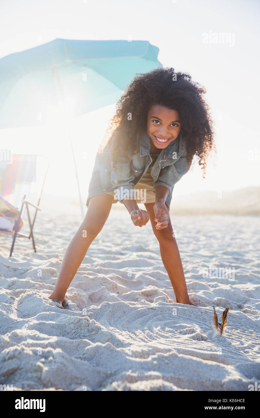 Portrait smiling, confident pre-adolescent girl bending on sunny summer beach Stock Photo