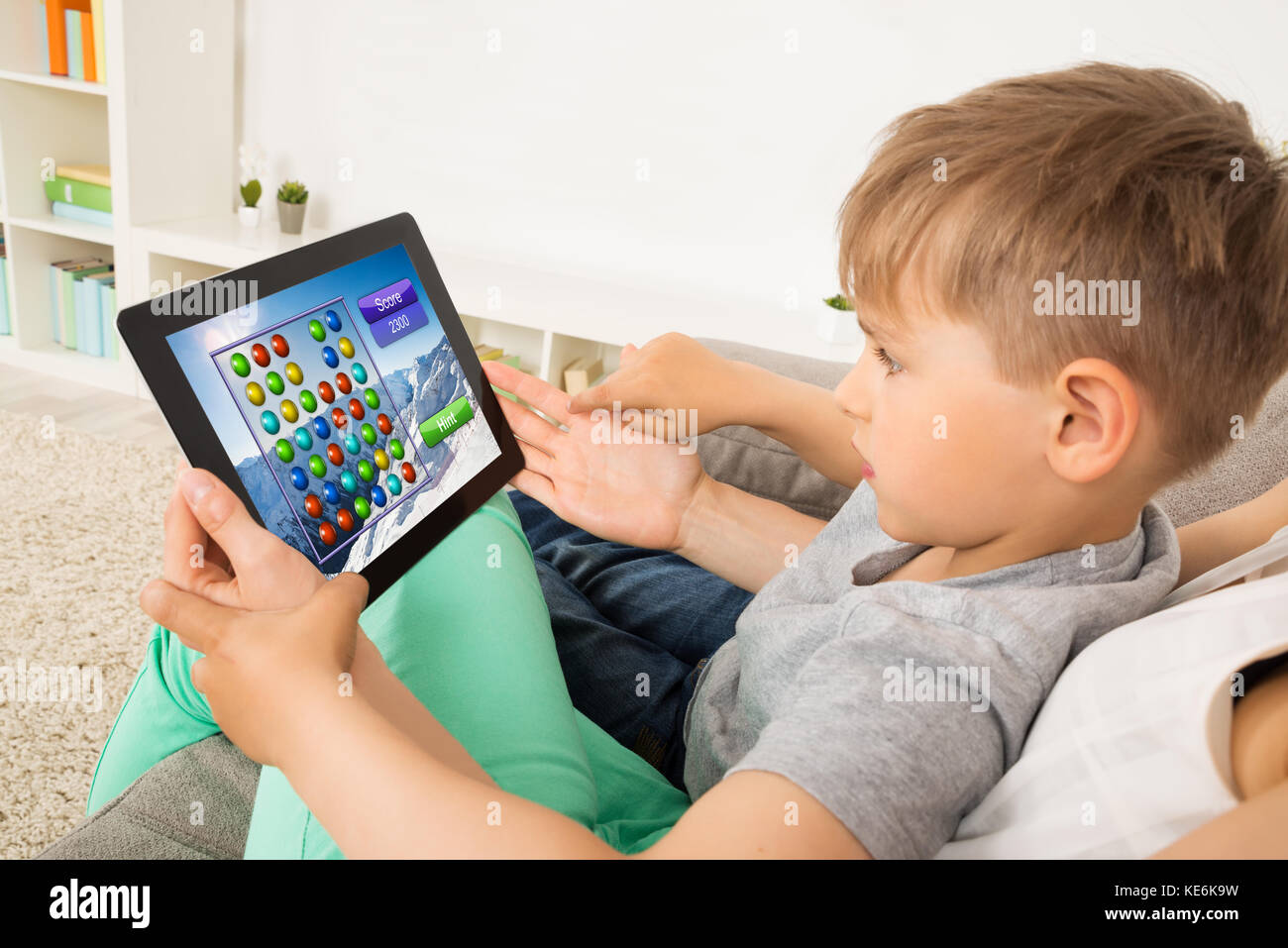 Little Child Sitting On Sofa Playing Game On Digital Tablet Stock Photo