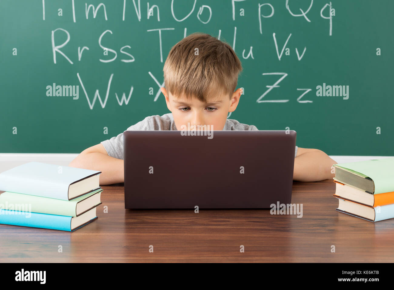 Boy Using Laptop In Front Of Green Chalkboard At School Stock Photo - Alamy