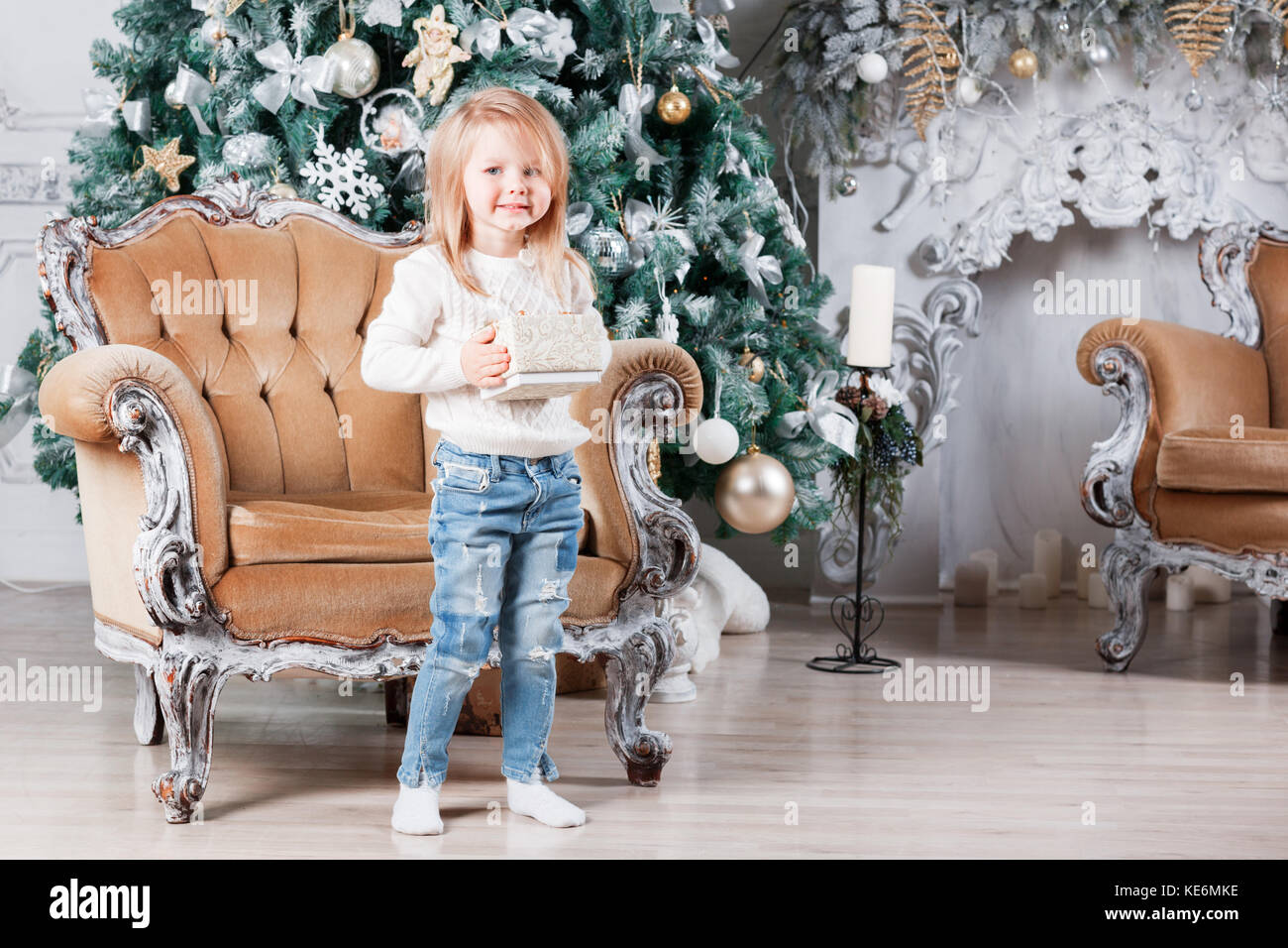 cute little girl sitting in a chair and opens a box with a present for ...