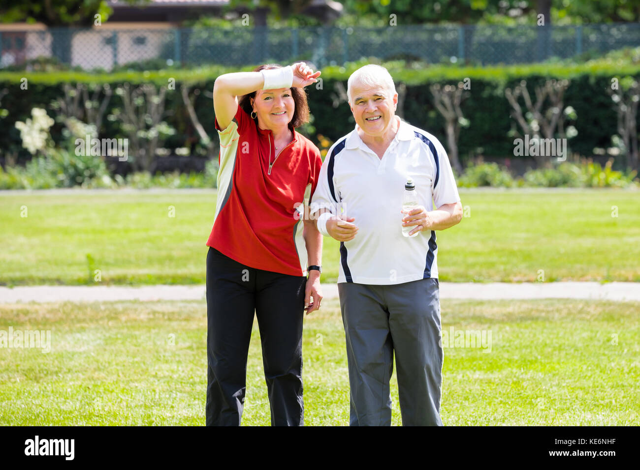 Tired Senior Couple Standing In Park Holding Bottle Of Water Stock Photo