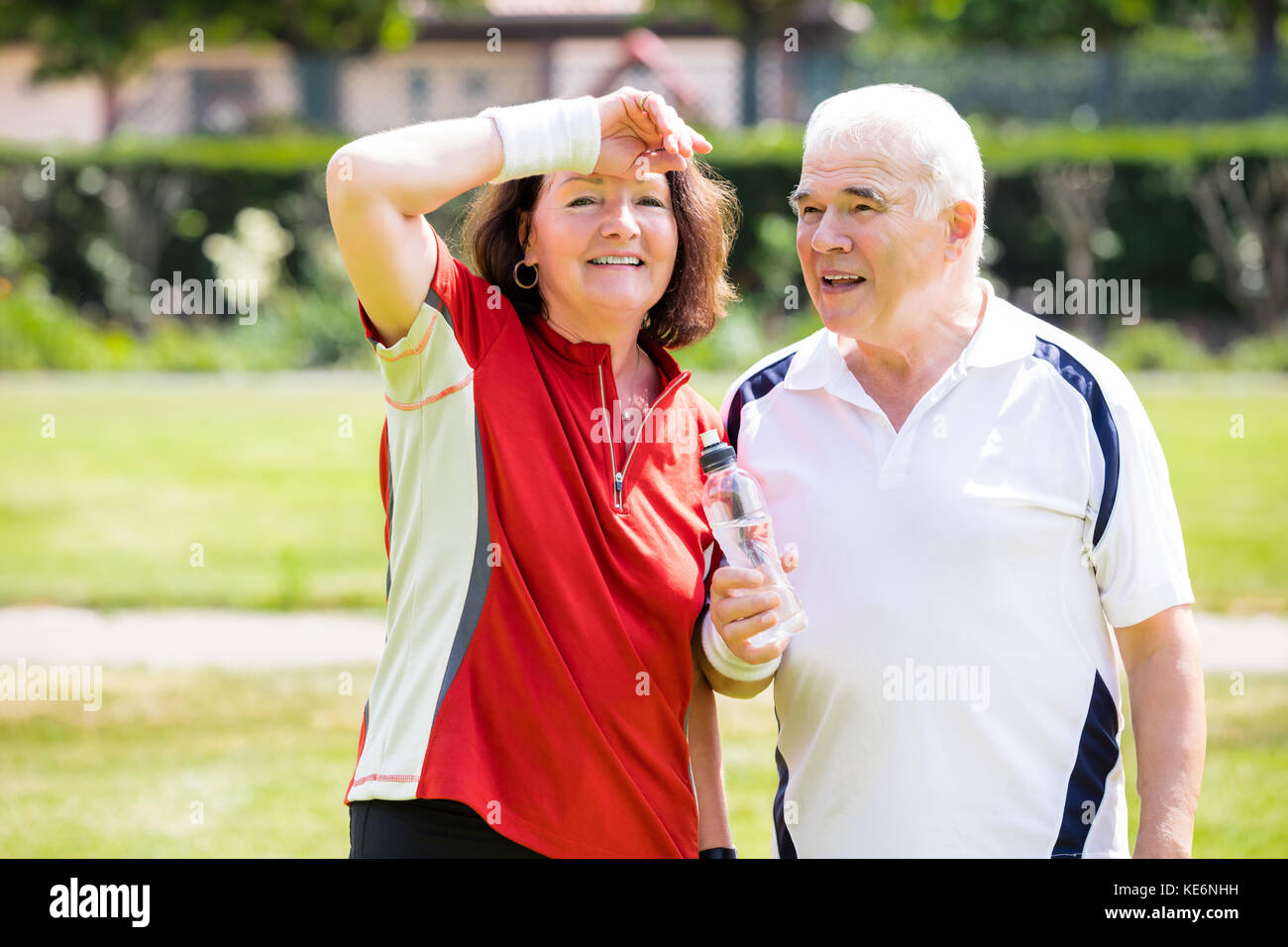 Tired Senior Couple Standing In Park Holding Bottle Of Water Stock Photo