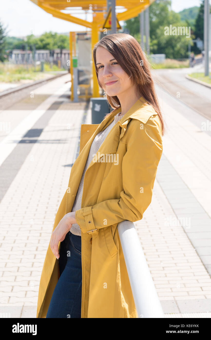 Young woman in a yellow raincoat waiting for a train at a railway station Stock Photo