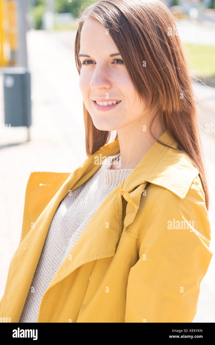 Young woman in a yellow raincoat waiting for a train at a railway station Stock Photo