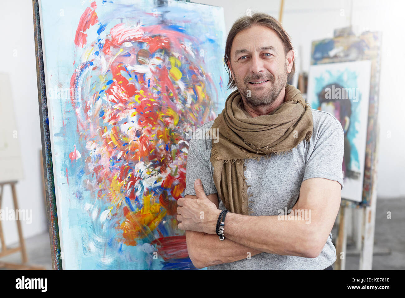 Portrait smiling, confident artist standing at abstract painting in art class studio Stock Photo