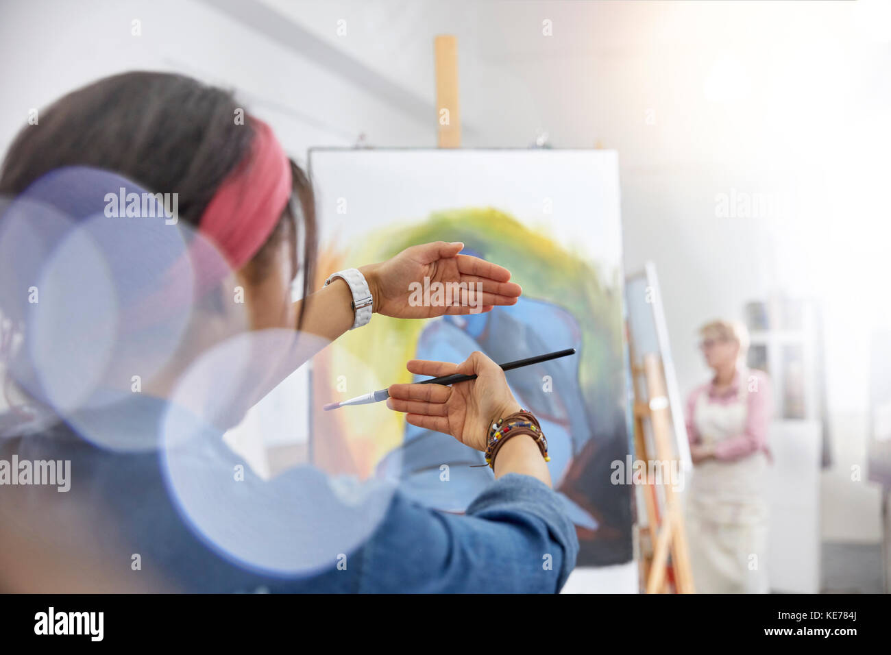 Female artist gesturing, framing painting on easel in art class studio Stock Photo
