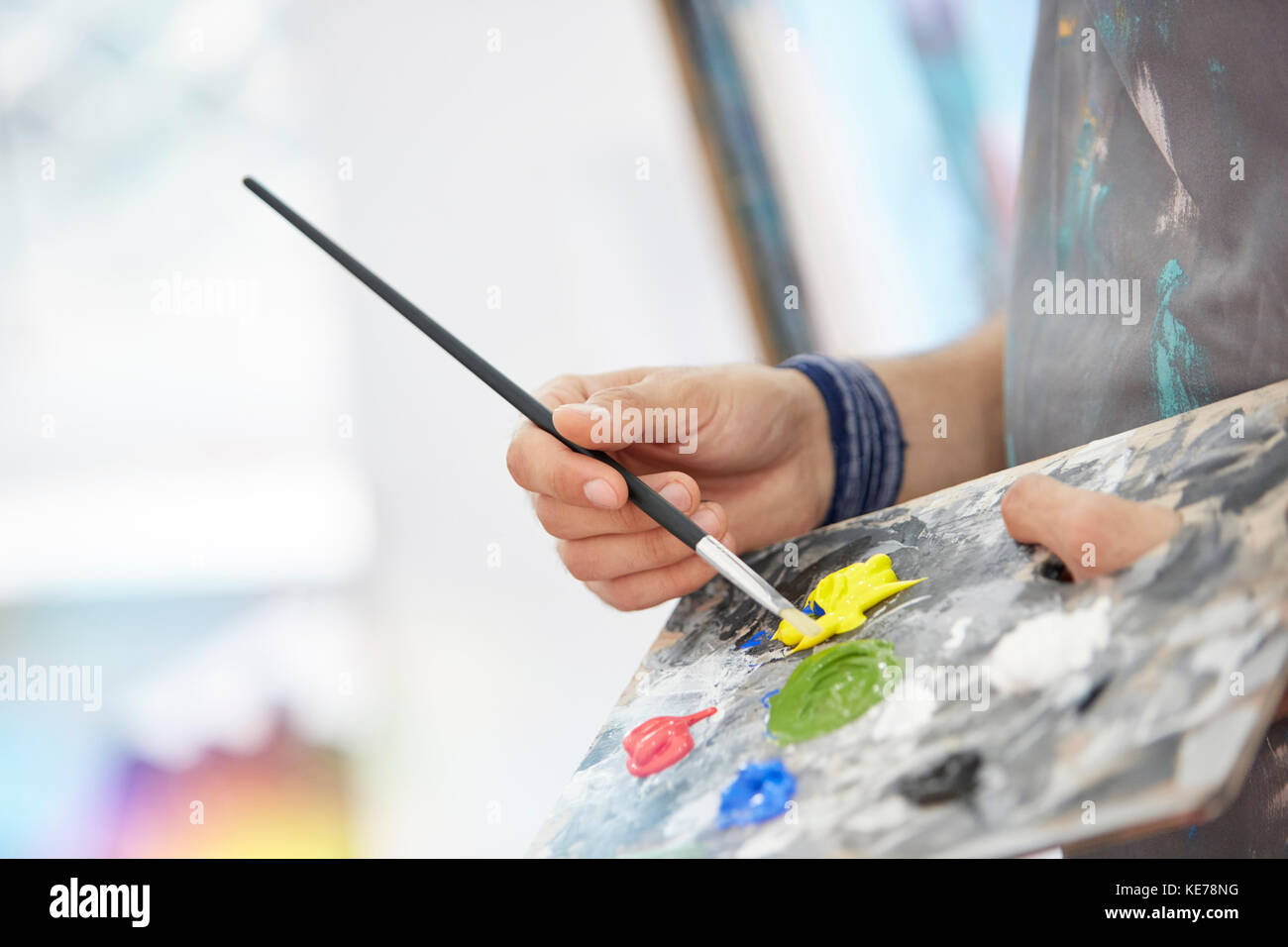 Close up artist dipping paintbrush in yellow paint on palette Stock Photo