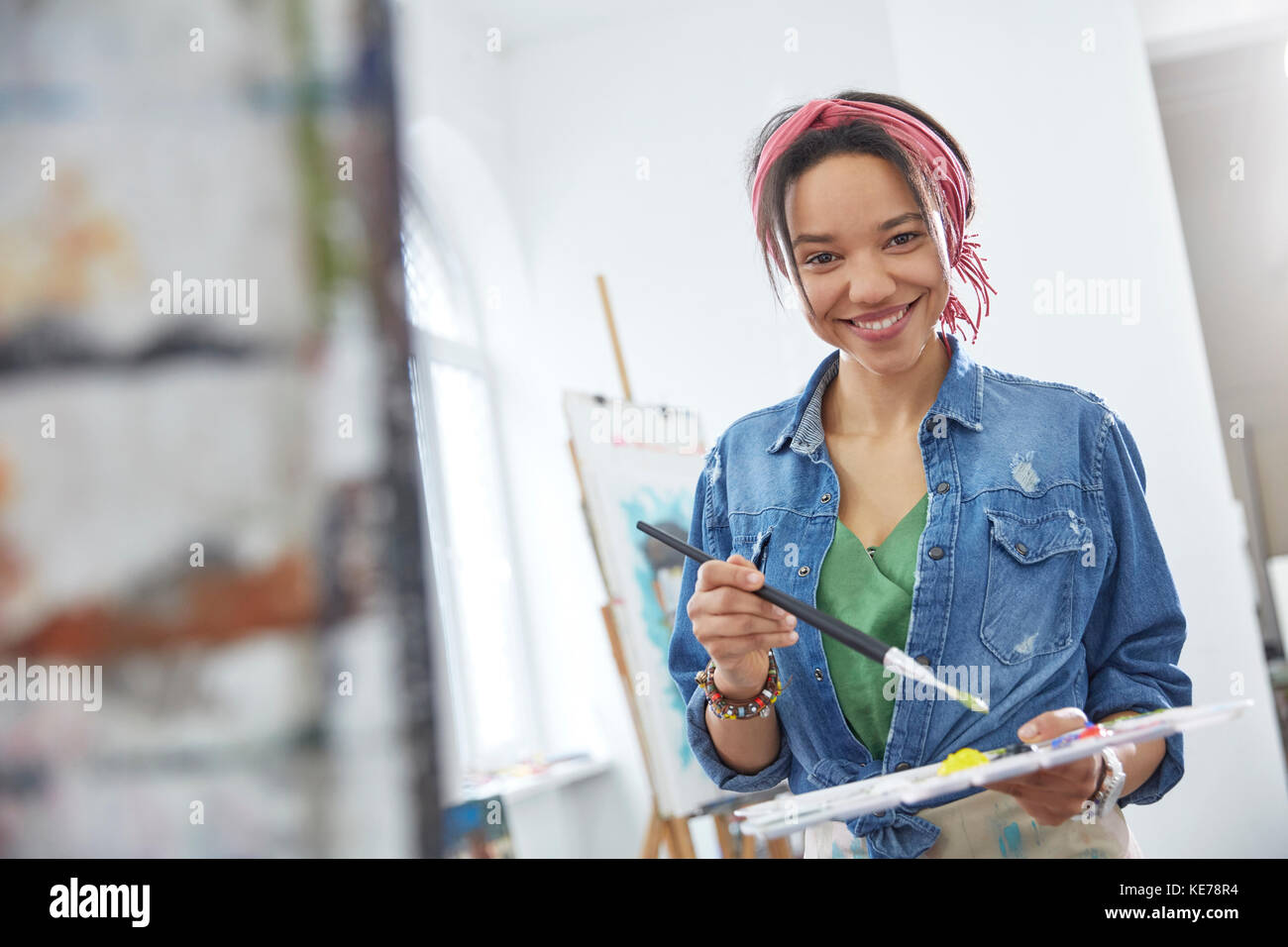 Portrait smiling female artist with paintbrush and palette, painting in ...
