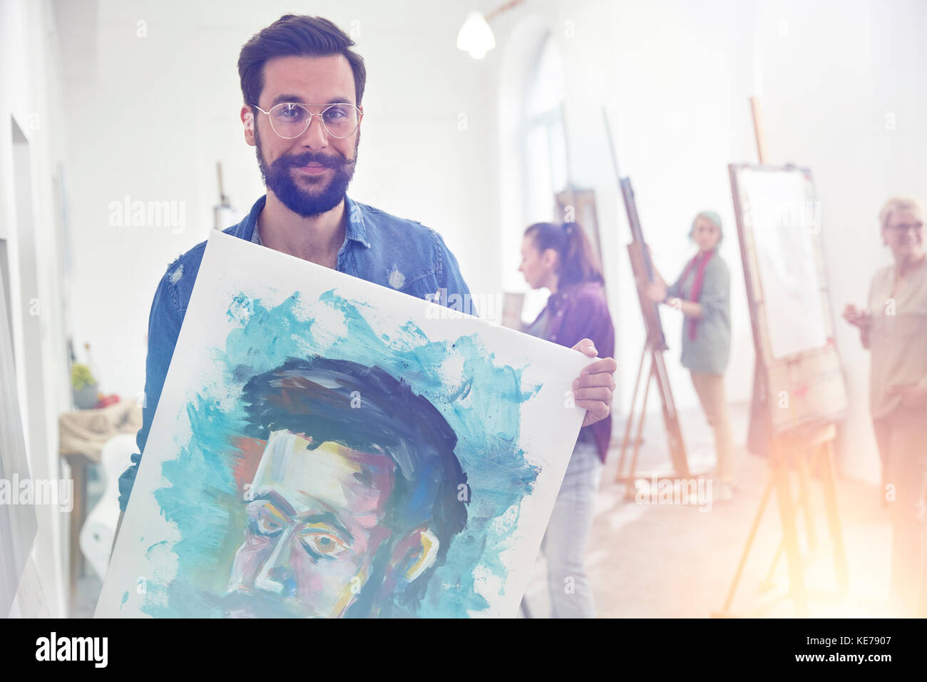 Portrait smiling, confident, proud male artist holding painting in art class studio Stock Photo